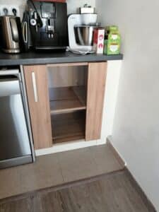 Cuisine moderne avec bouilloire argentée, cafetière Jura, robot pâtissier Bosch, thé Twinings et boîte Canderel sur plan de travail. Meuble bas vitré en bois.