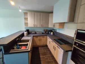 Cuisine moderne avec meubles bois clair, plans de travail sombres marbrés et murs bleu pâle. Évier, plaque induction, four et appareils.