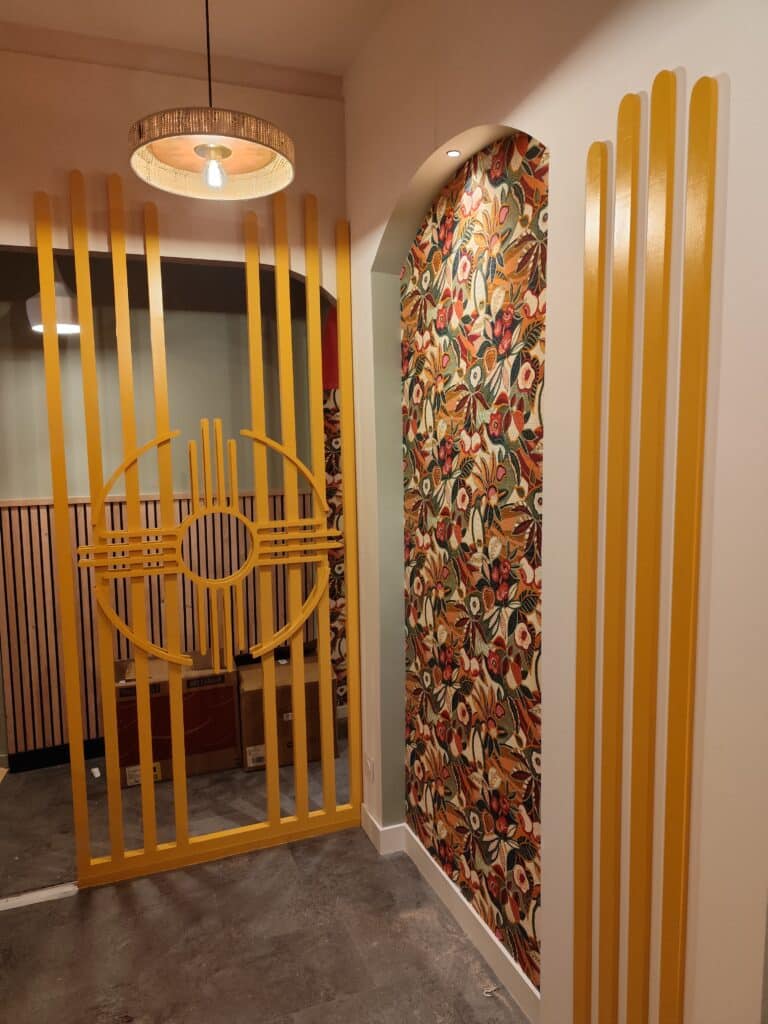 Décoration intérieure moderne avec cloison jaune à motifs circulaires, arche murale tapissée de motifs floraux vifs et lattes verticales jaunes.