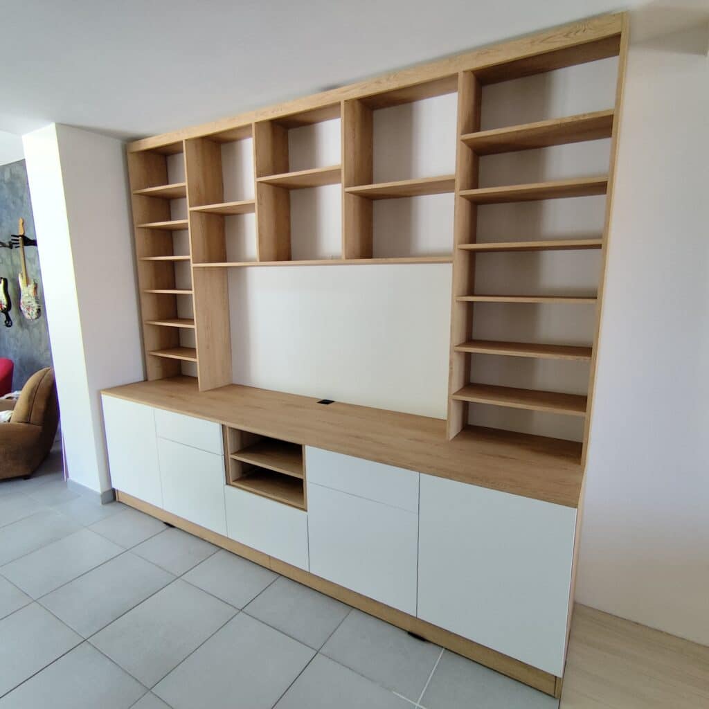 Meuble TV mural sur mesure, bois clair et blanc. Étagères intégrées et rangements bas fermés pour salon moderne.